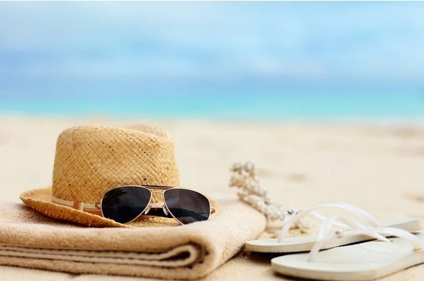 Zomerbeeld van handdoek, slippers, zonnebril en hoedje op het strand met zee en blauwe lucht – symbool voor het vakantiegevoel